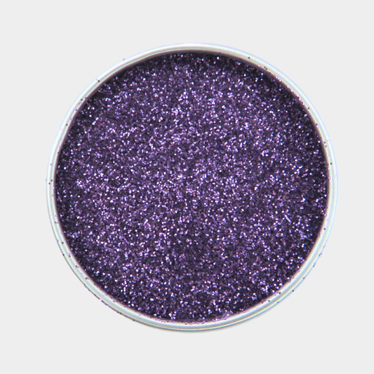 Purple glitter in a round container on a light gray background