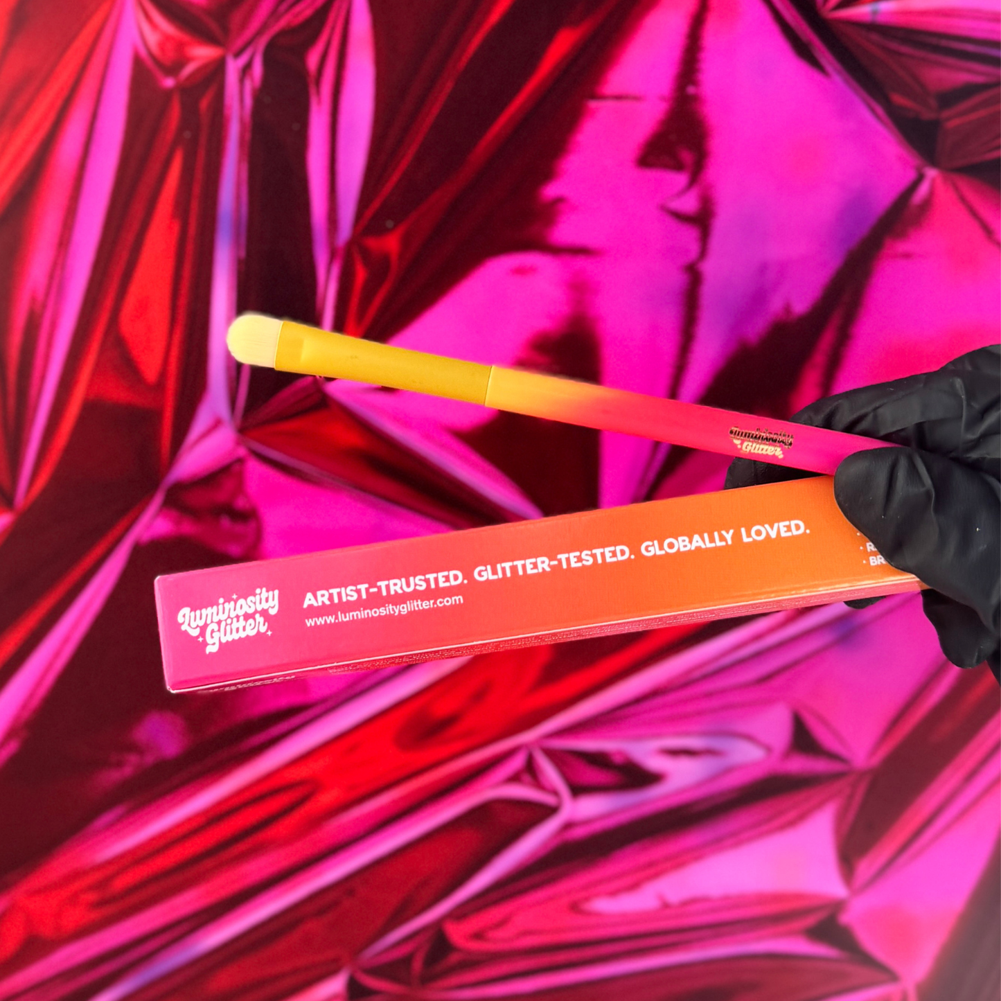 Orange makeup brush with text held against a pink reflective background