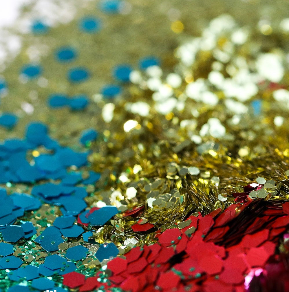Close-up of cosmetic glitter in multiple colors, including gold, red, pink, blue, and green, with two small clear jars filled with glitter on a reflective surface. A logo in the lower left reads 'Cosmetic Bio-glitter SPARKLE' and '© Righton Button Ltd'.