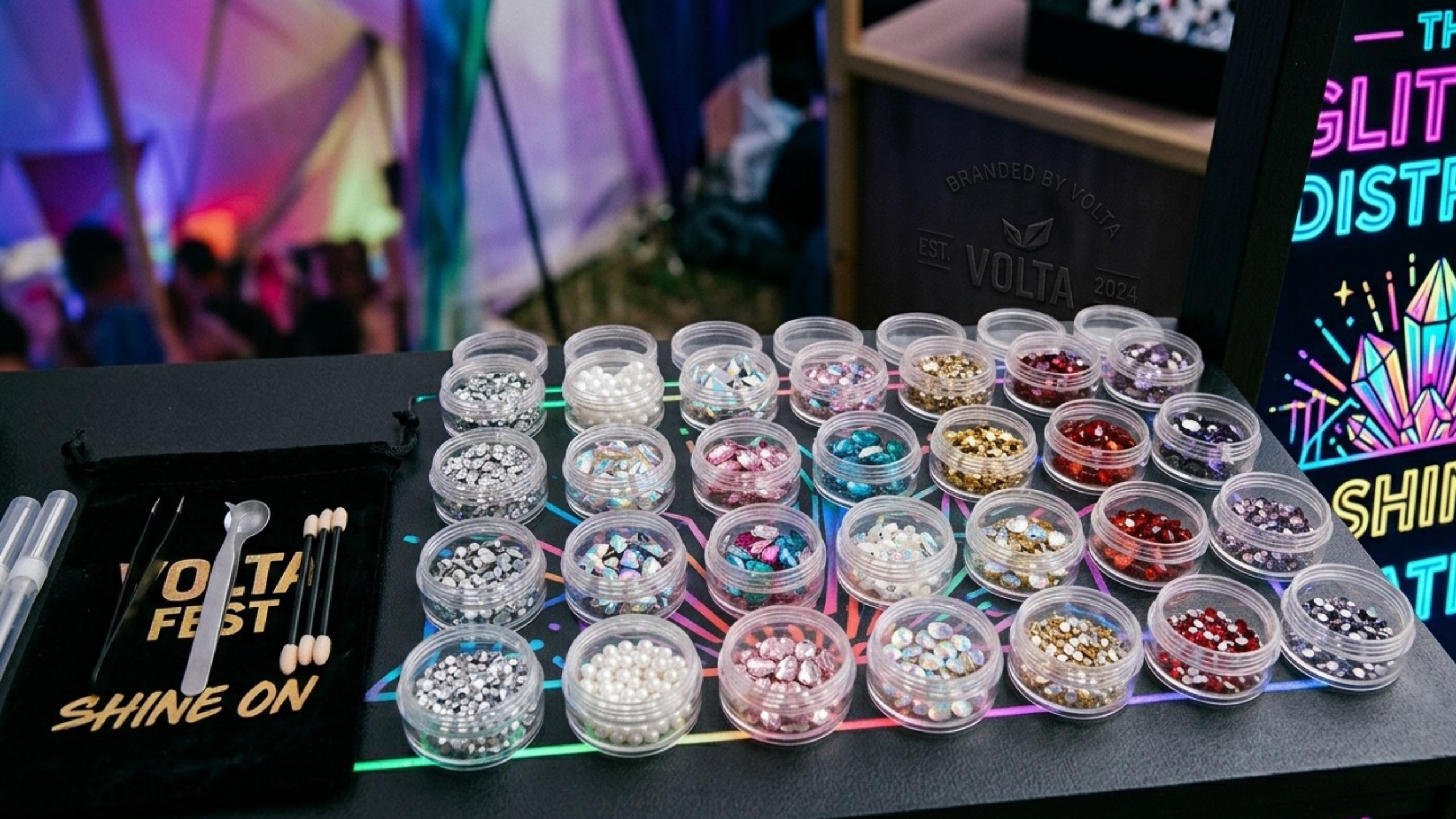 Assorted small containers with colorful loose face gems on a table with event branding in the background