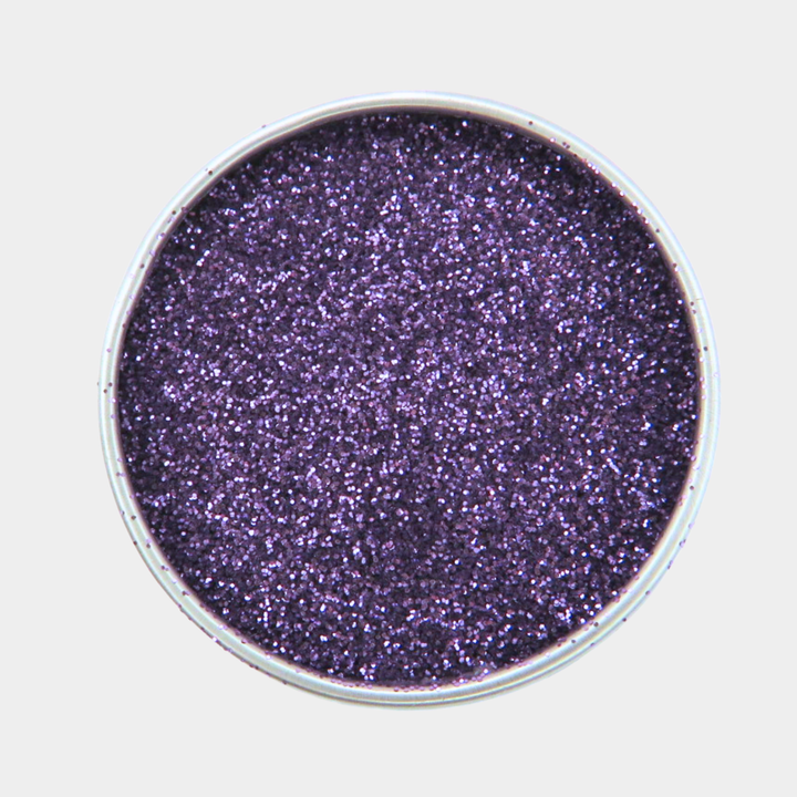 Purple glitter in a round container on a light gray background