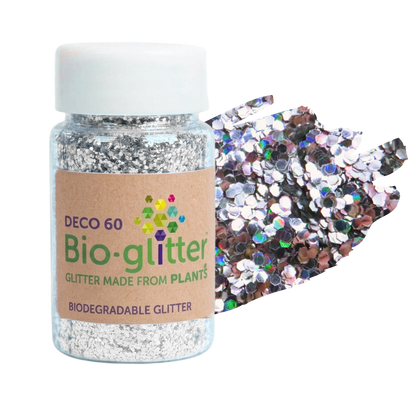 A jar of silver chunky craft bio-glitter with a white cap and a kraft paper label, shown next to a pile of iridescent silver sequins on a white background.